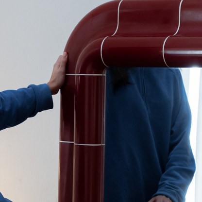 Lola Mirror in Deep Burgundy reflected in a contemporary interior with a person standing nearby.